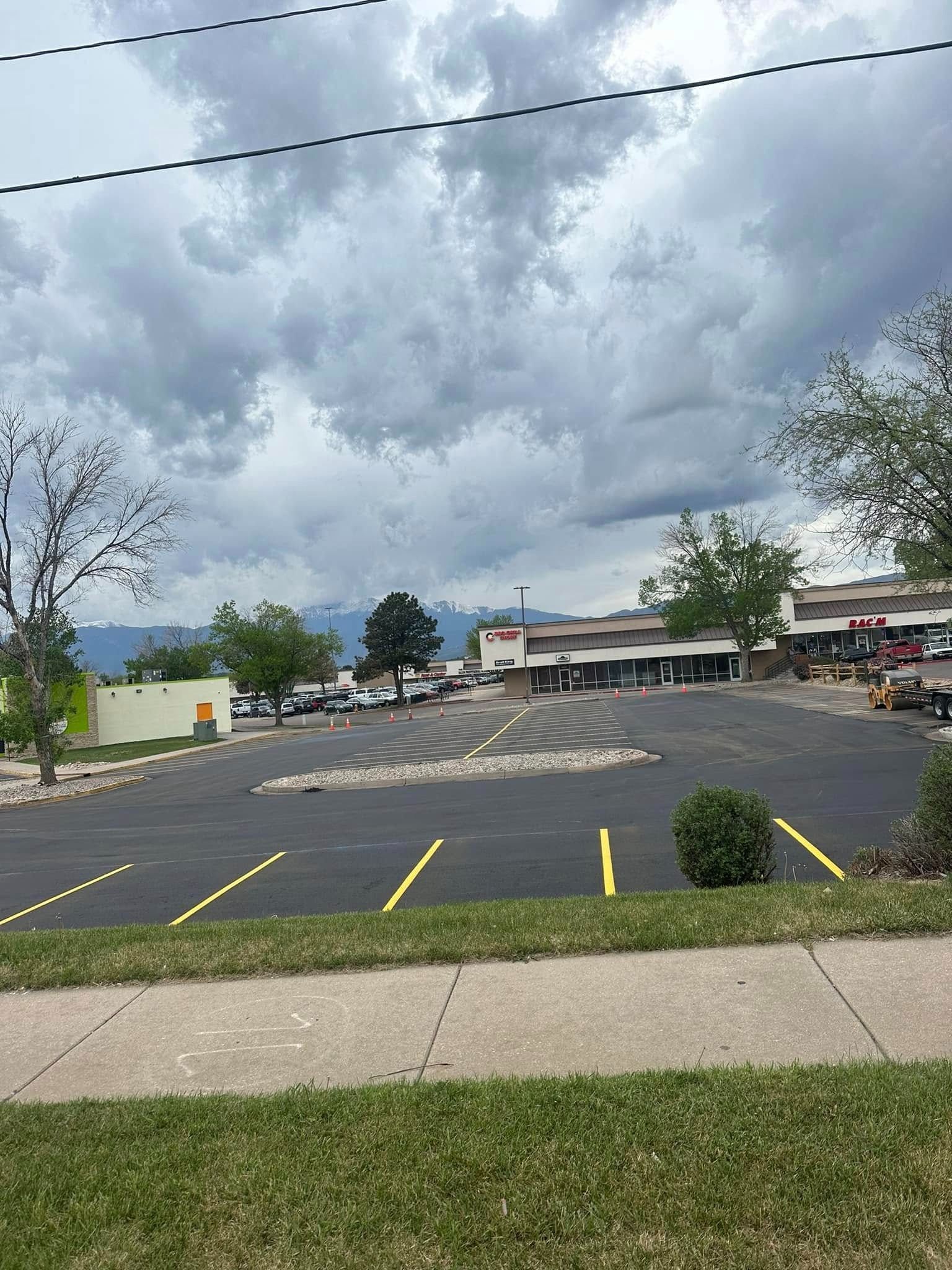 Black asphalt parking lot with yellow lines. Cloudy sky over a small commercial area.
