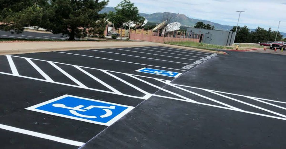 Asphalt parking lot with painted white and blue accessibility markings, including wheelchair symbols.