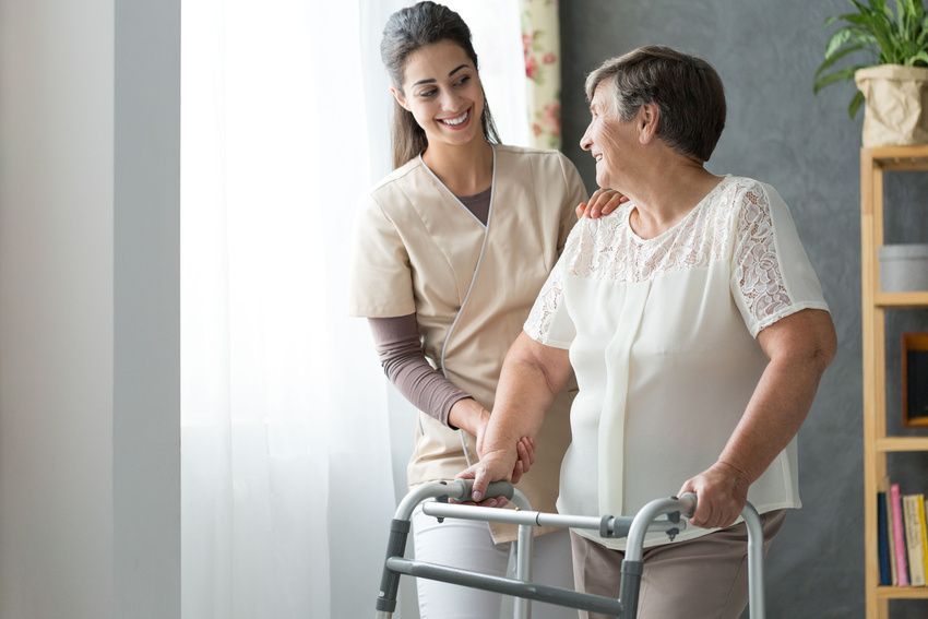 Caregiver assisting a smiling woman with a walker in a bright home setting