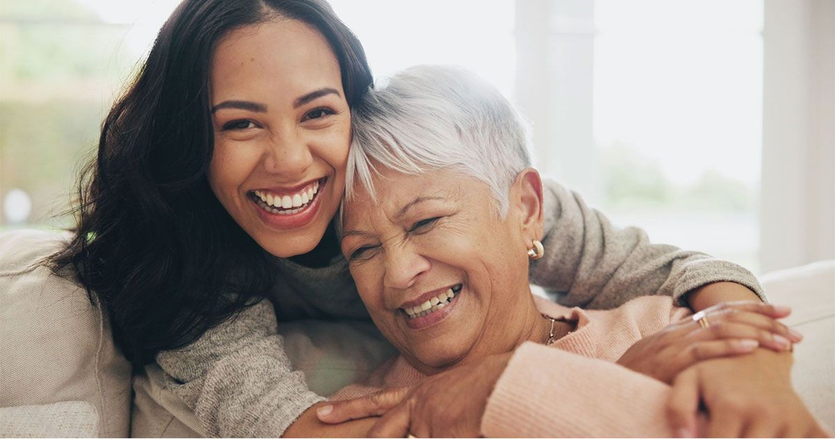 Two people smiling and hugging on a light-colored couch in a bright living room