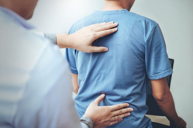 The doctor examines a man's back, pressing with his hands. Setting: clinic. Focus on pain evaluation.