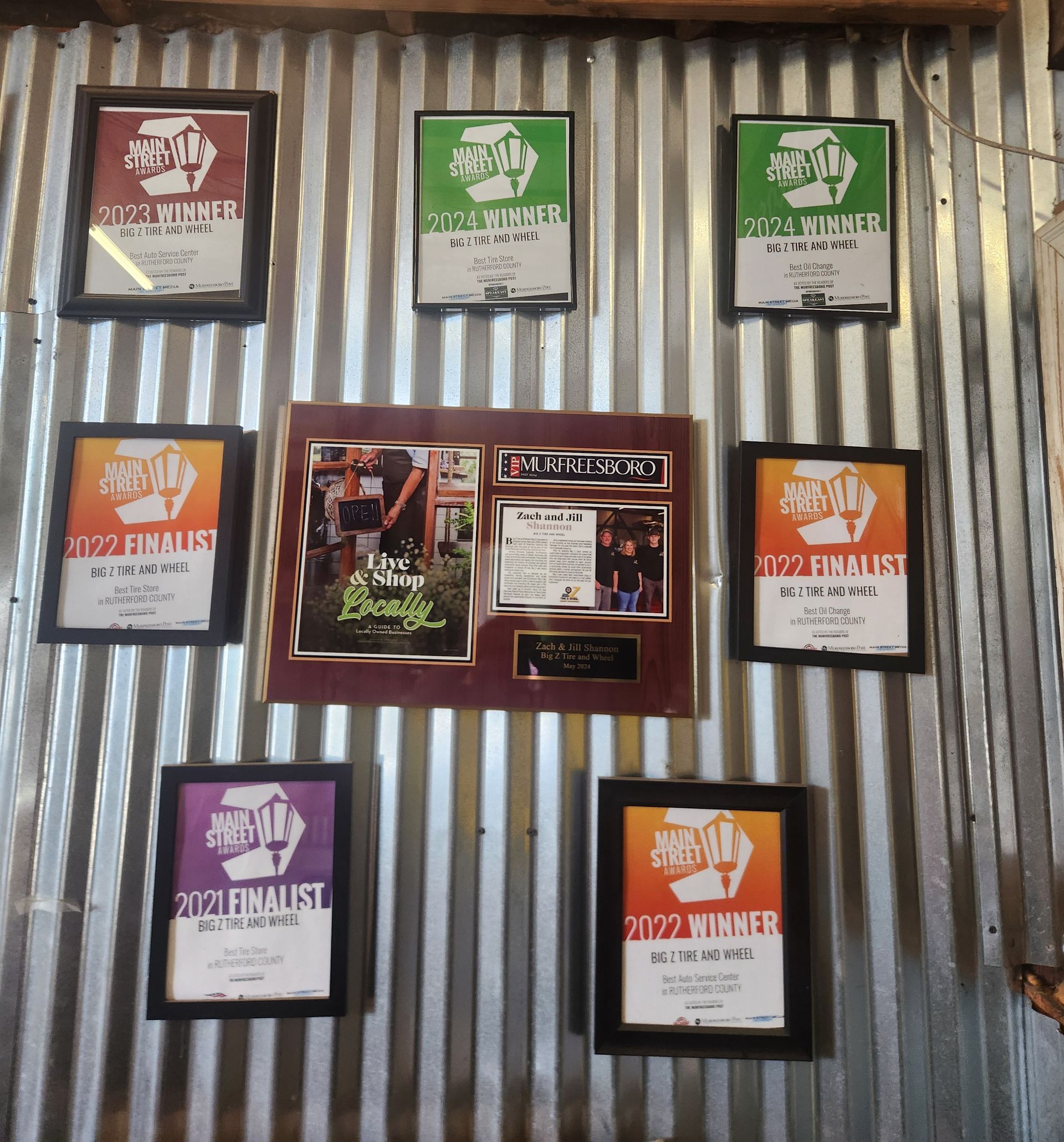 Flyers and posters in colorful frames displayed on a corrugated metal wall.