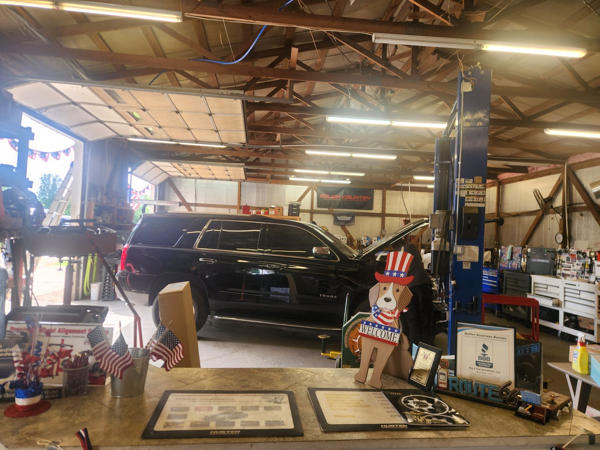 Black SUV in a garage with tools, posters, and a lift under warm overhead lights