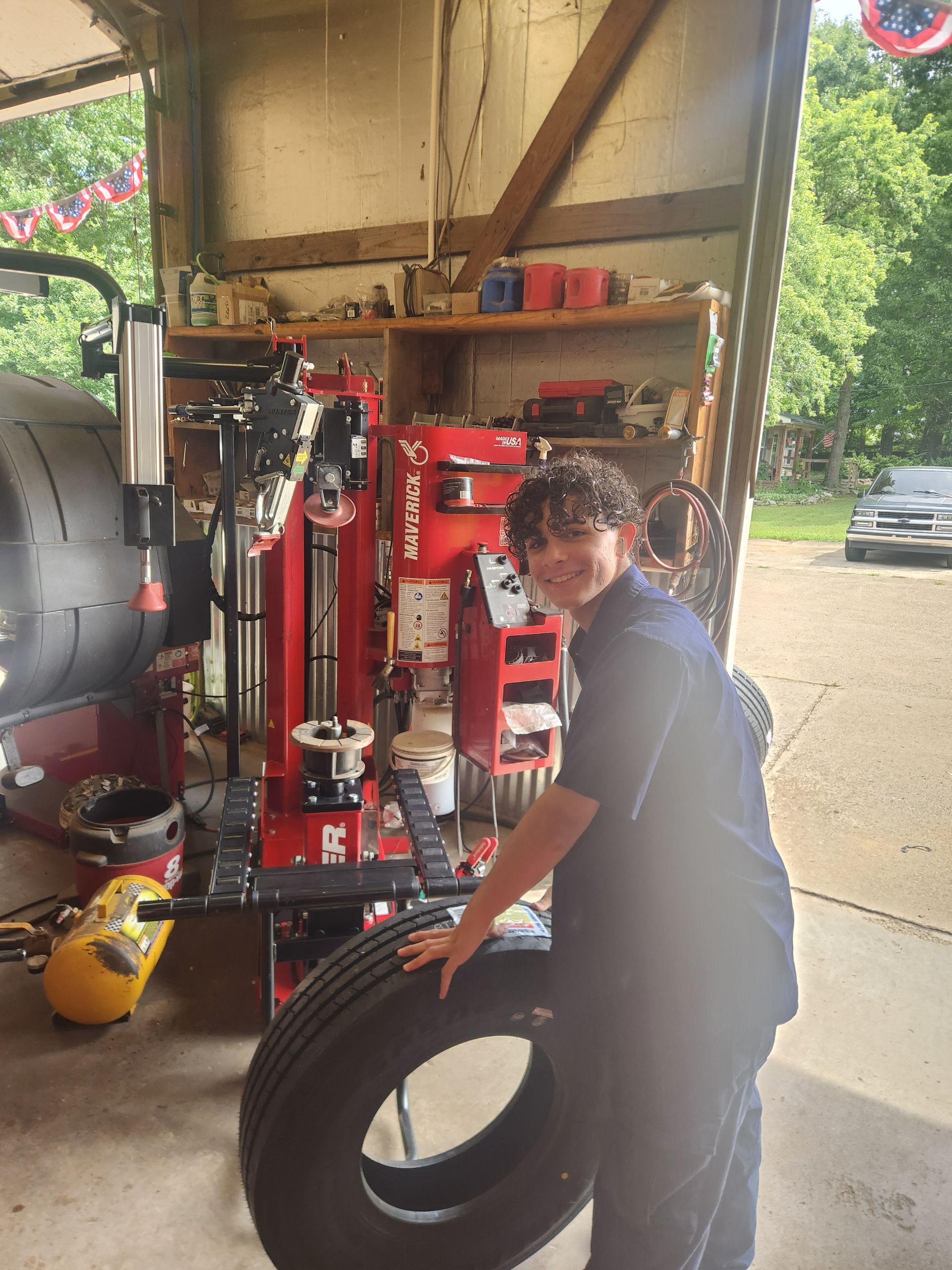 Person holding a large tire in a garage beside a red tire-changing machine