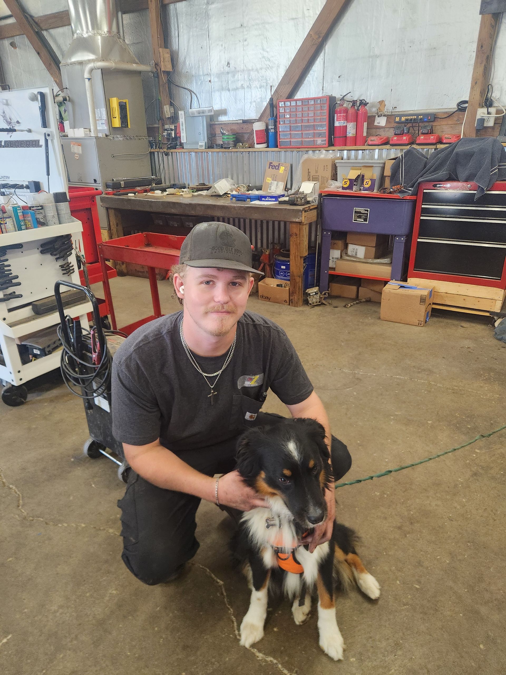Person kneeling with a black, white, and orange dog in a workshop.