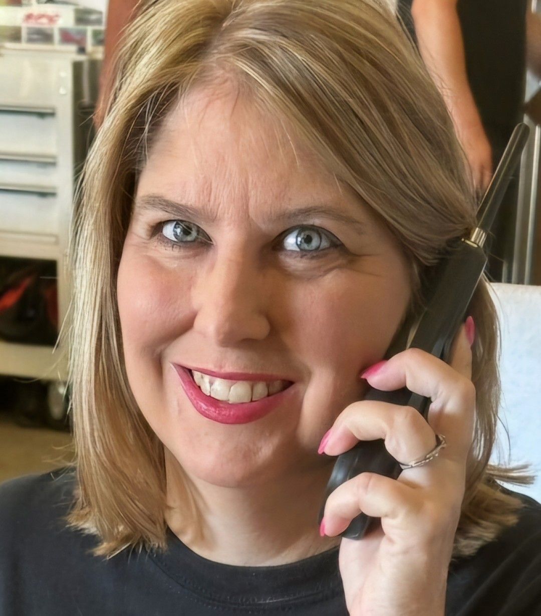 Smiling woman holding a phone to her ear, with a black shirt and pink lipstick.