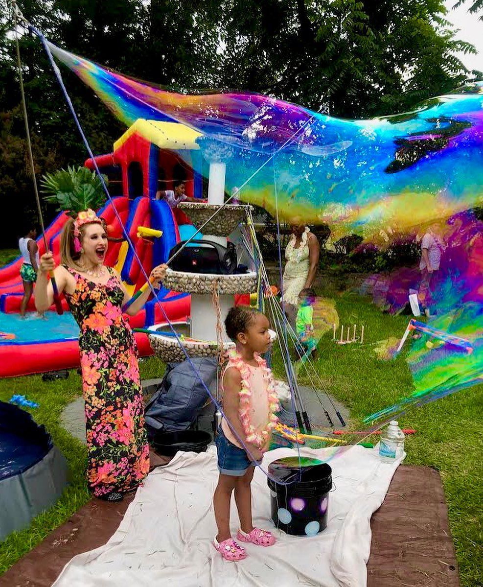 A woman and a little girl are playing with giant soap bubbles in a backyard.
