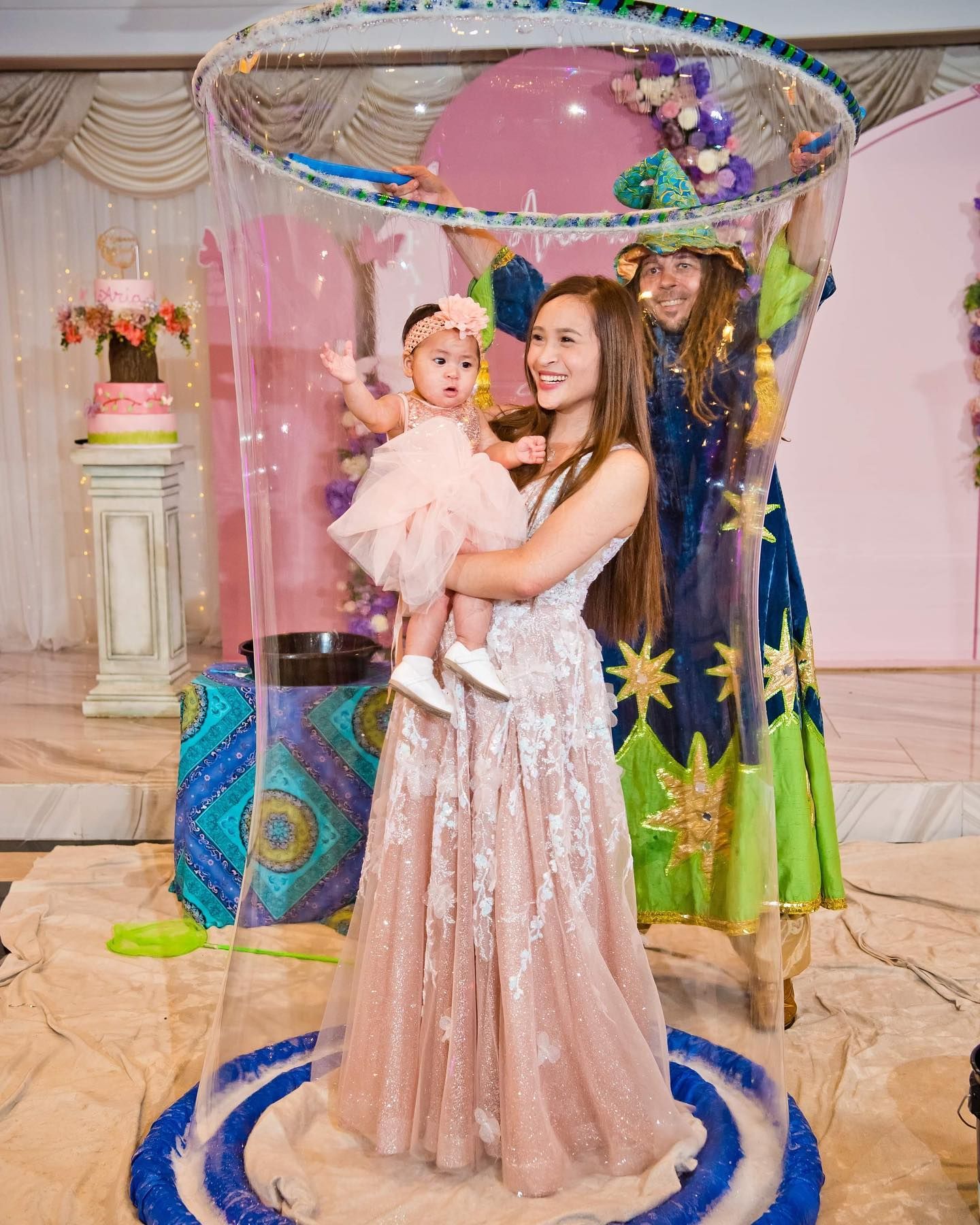 A woman in a long dress is holding a baby in a bubble.