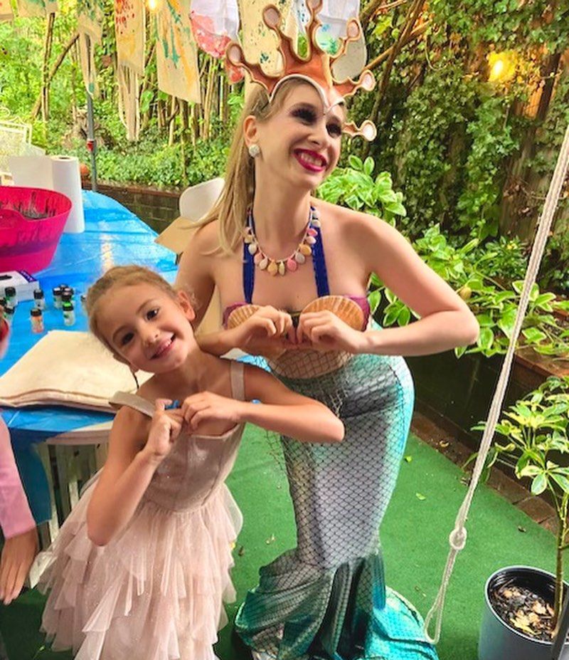 A woman in a mermaid costume is standing next to a little girl in a pink dress.