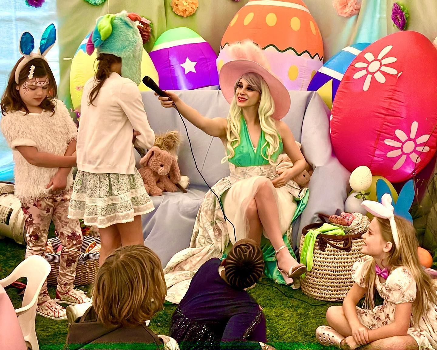 A woman is sitting on a couch talking to a group of children.