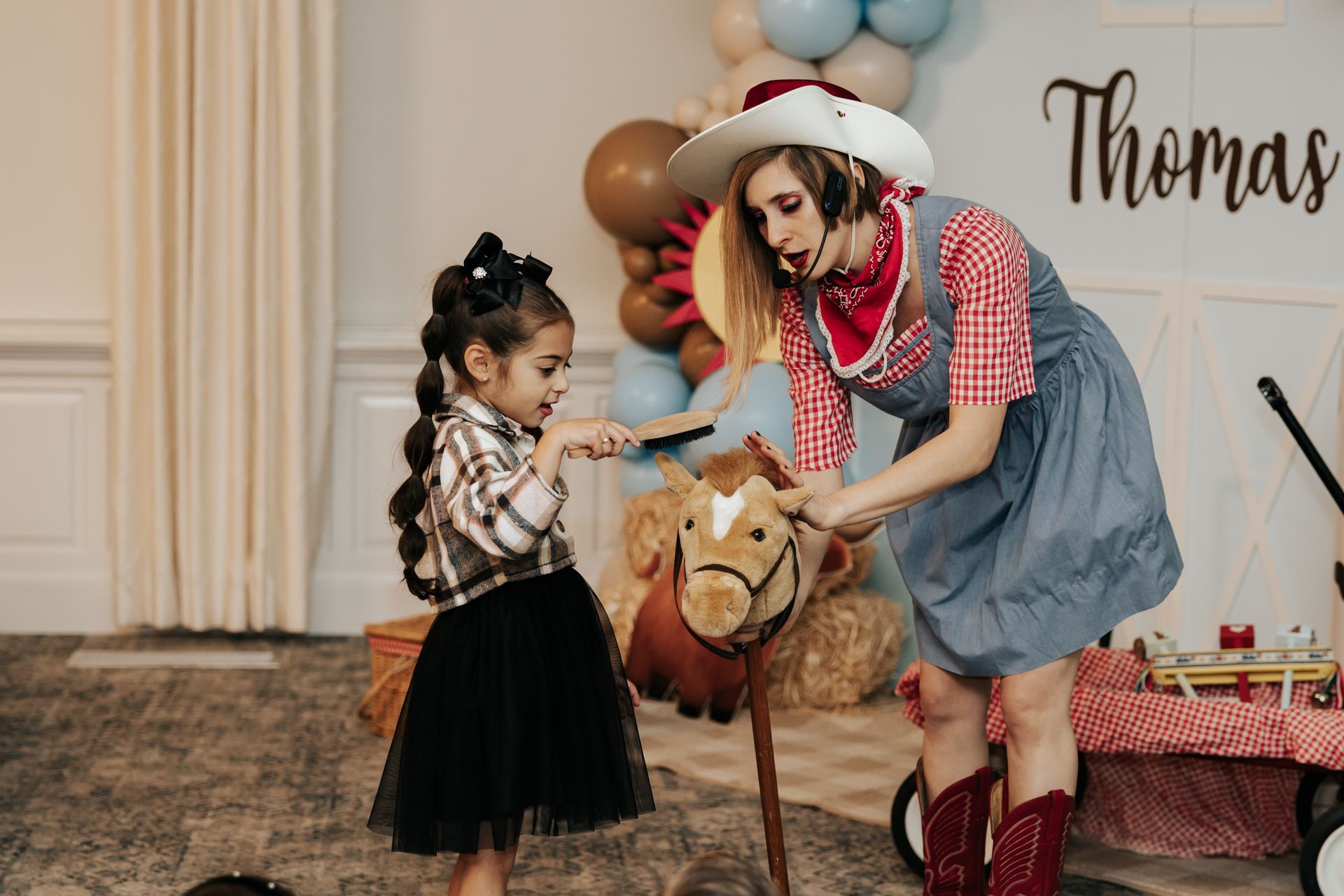 A woman dressed as a cowboy is playing with a little girl on a rocking horse.