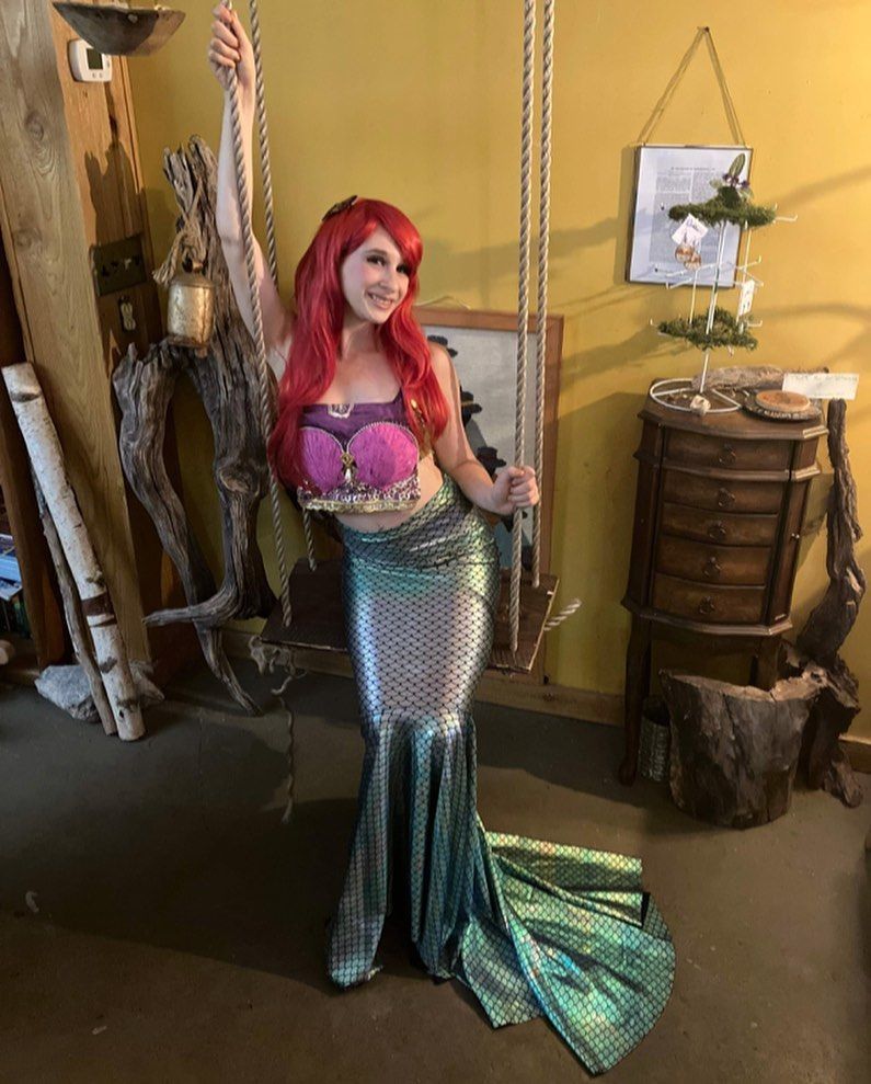 A woman in a mermaid costume is standing on a swing in a room.