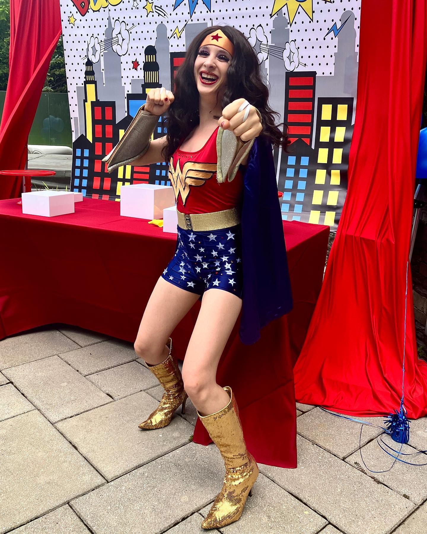 A woman in a wonder woman costume is standing in front of a table.