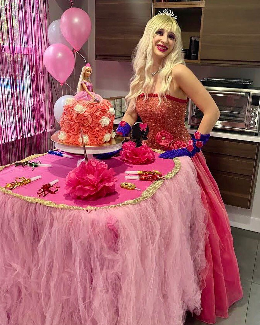 A woman in a pink dress is standing in front of a table with a cake on it.