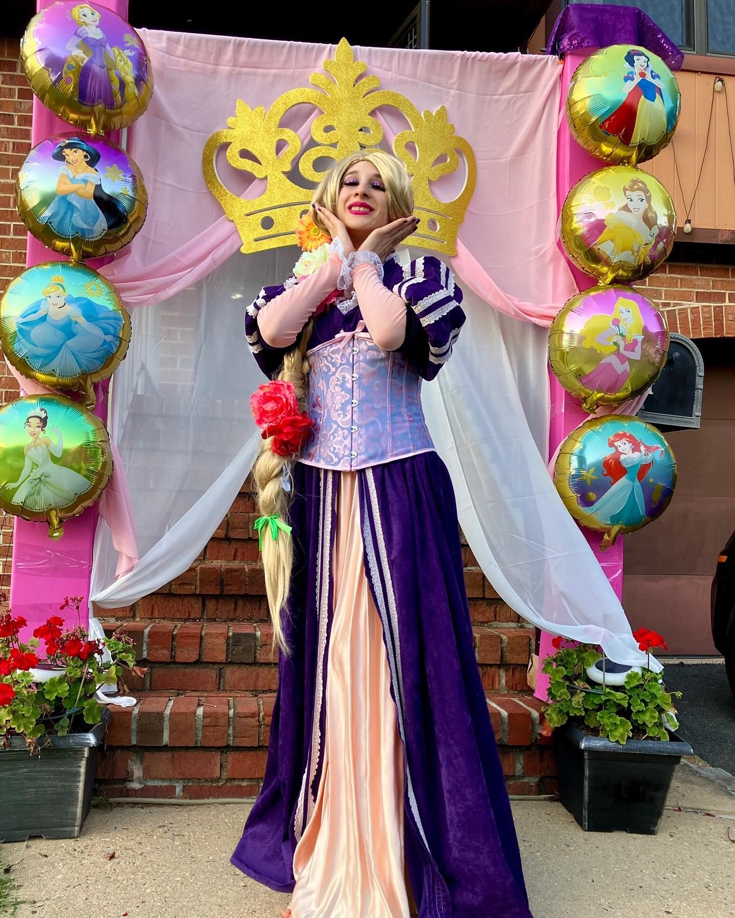 A woman dressed as rapunzel is standing in front of a display of princess balloons.