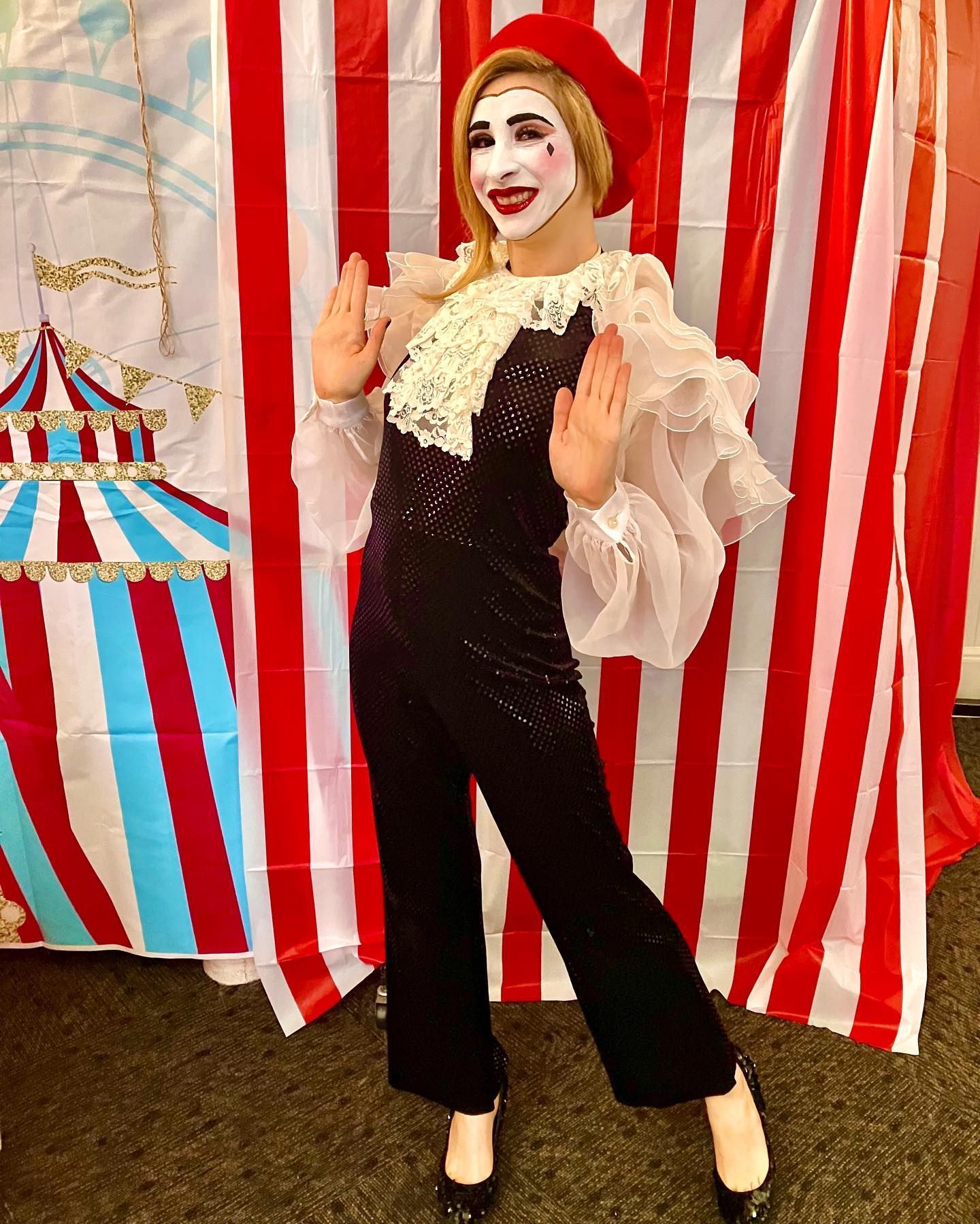 A woman in a clown costume is standing in front of a striped curtain.