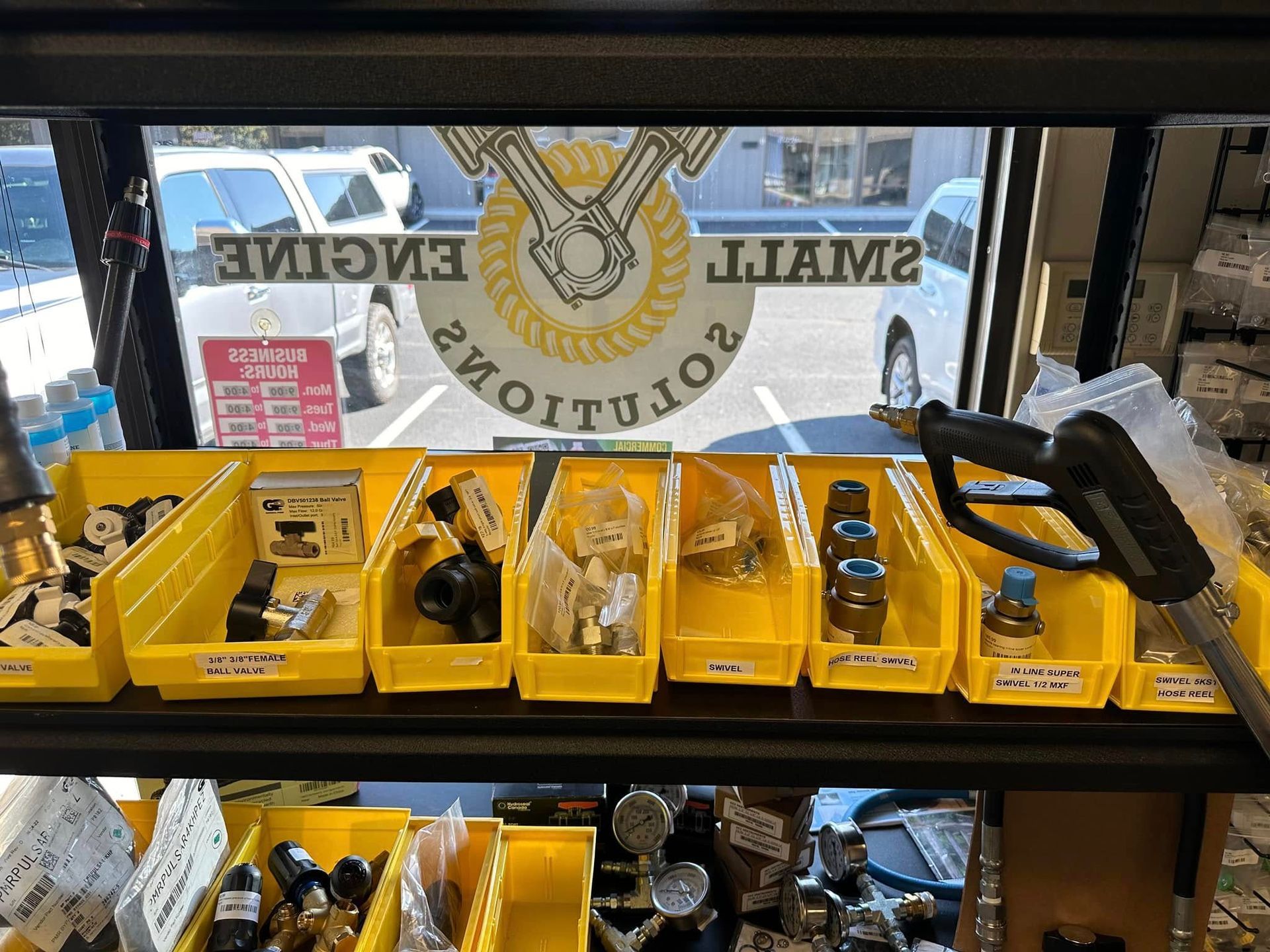 Shelves with yellow bins of small engine parts inside a store window with logo: 