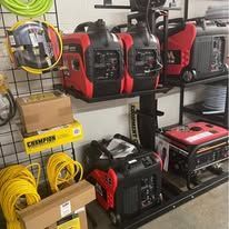 Red generators on a shelving unit at a hardware store, with yellow extension cords.