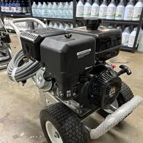Black and silver pressure washer on wheels with an engine, in a workshop setting.