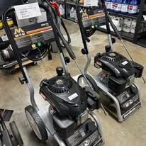 Three pressure washers on a store floor; two are black and silver, and one is partially visible.