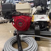 A red and black pressure washer engine with a coiled grey hose on the floor.