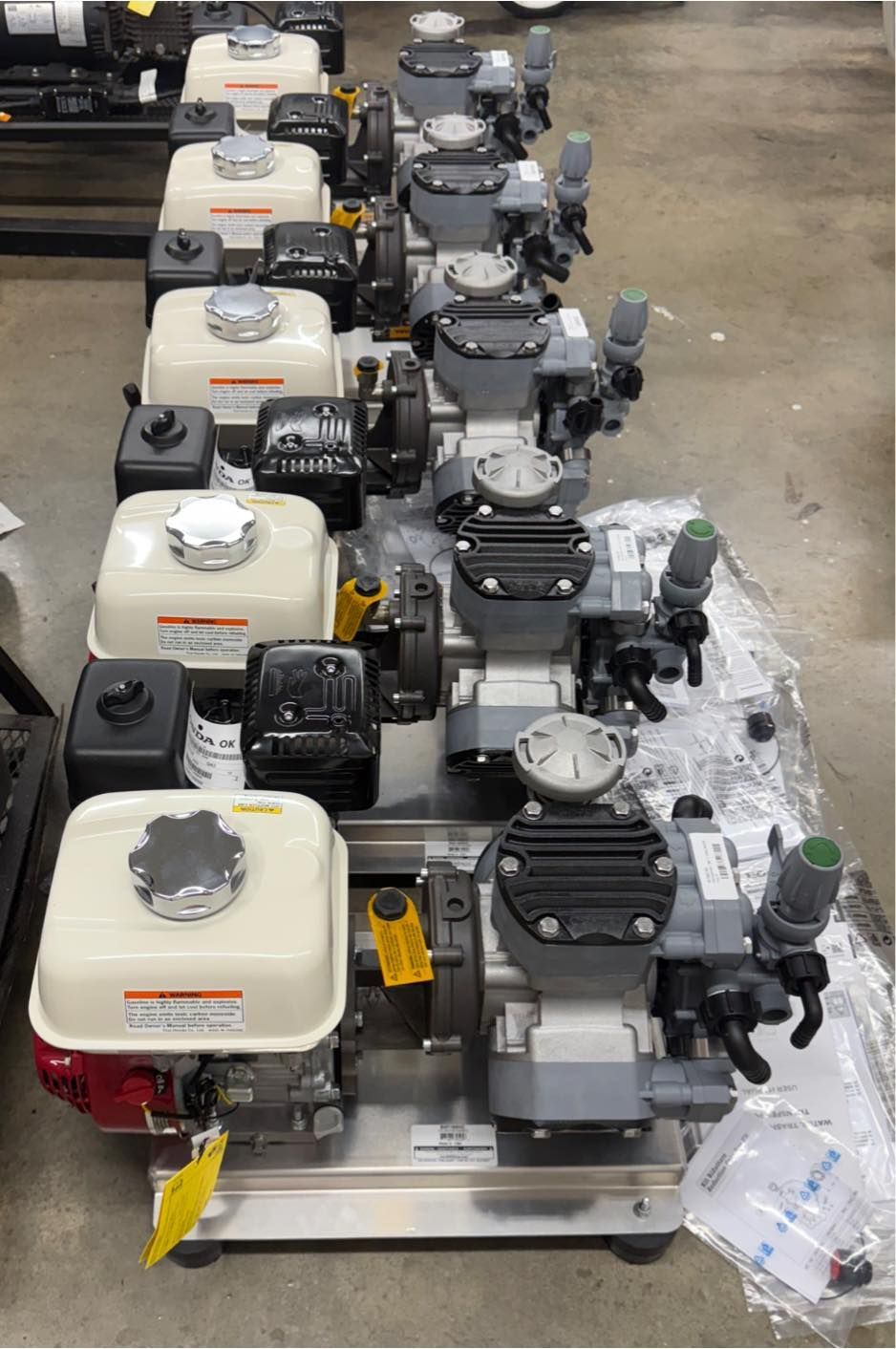 Row of new gasoline powered water pumps, beige engines, gray pump units, silver fuel caps.
