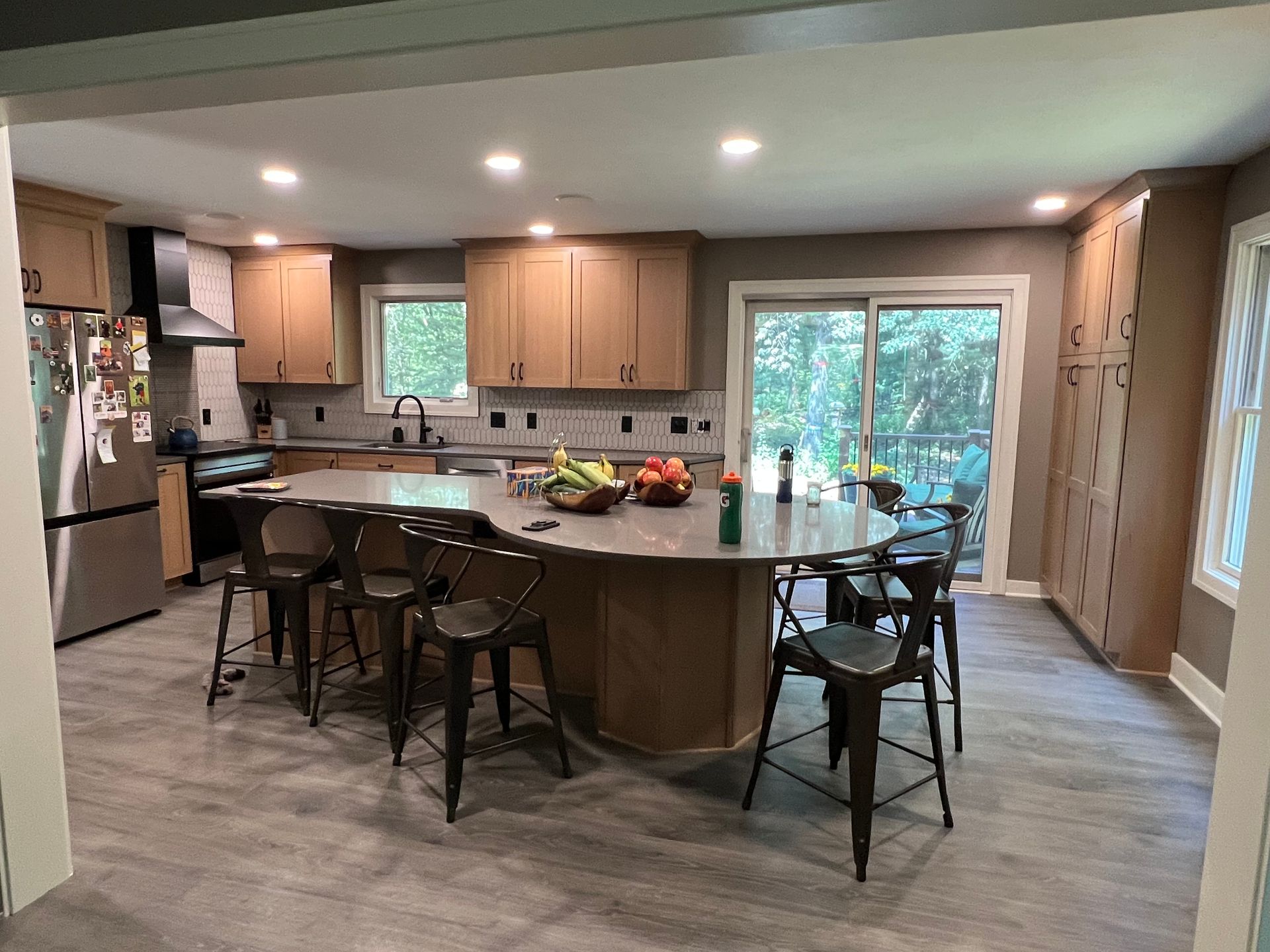 Modern kitchen with large island, stools, and light-colored cabinets, gray flooring.