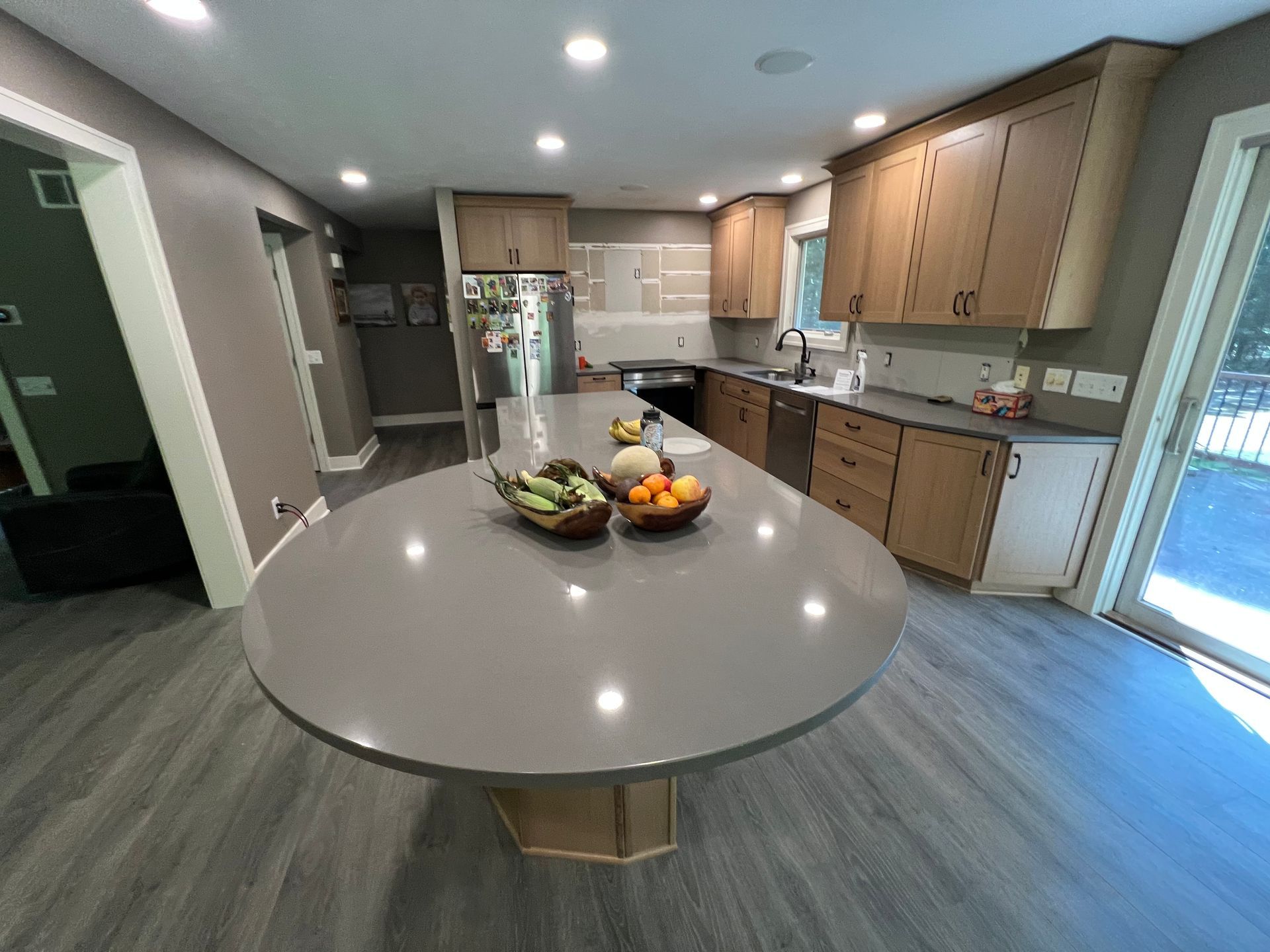 Kitchen with large gray island, light wood cabinets, and gray flooring.