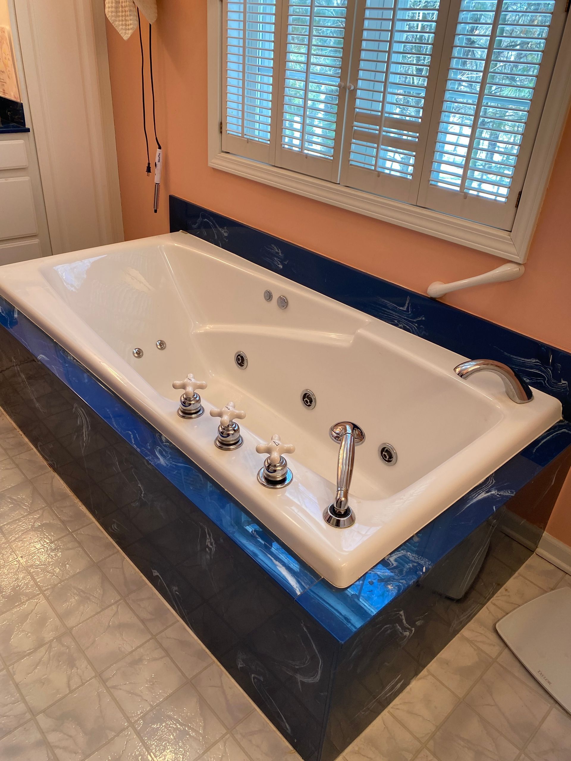 Jacuzzi bathtub with chrome fixtures, next to a window with blinds, in a bathroom.