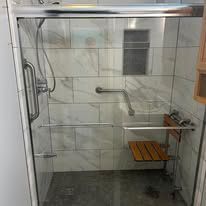A bathroom with a sliding glass shower door and a wooden seat.