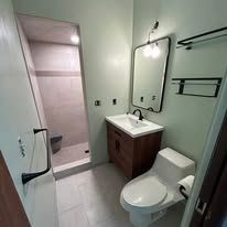 A bathroom with a toilet , sink , mirror and shower.