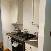 A kitchen with white cabinets , a stove , and a kettle on the stove.