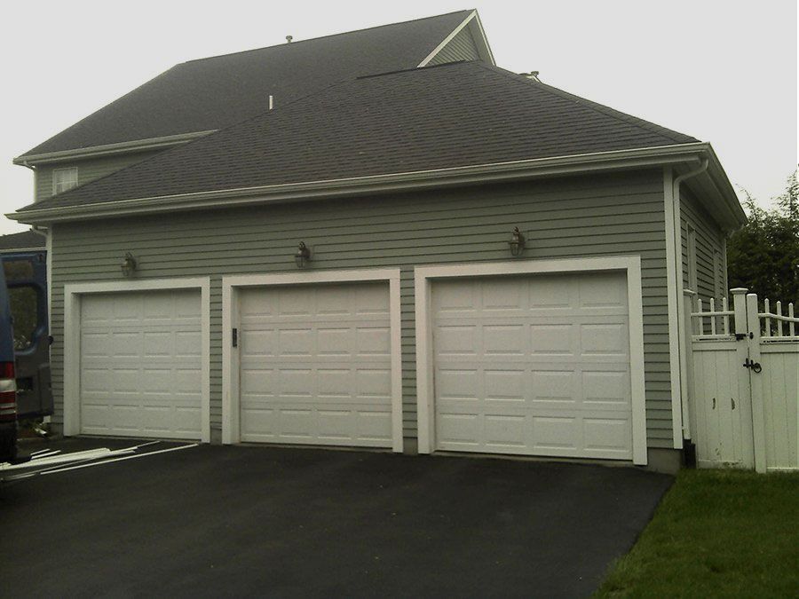 A garage with three white garage doors and a black roof