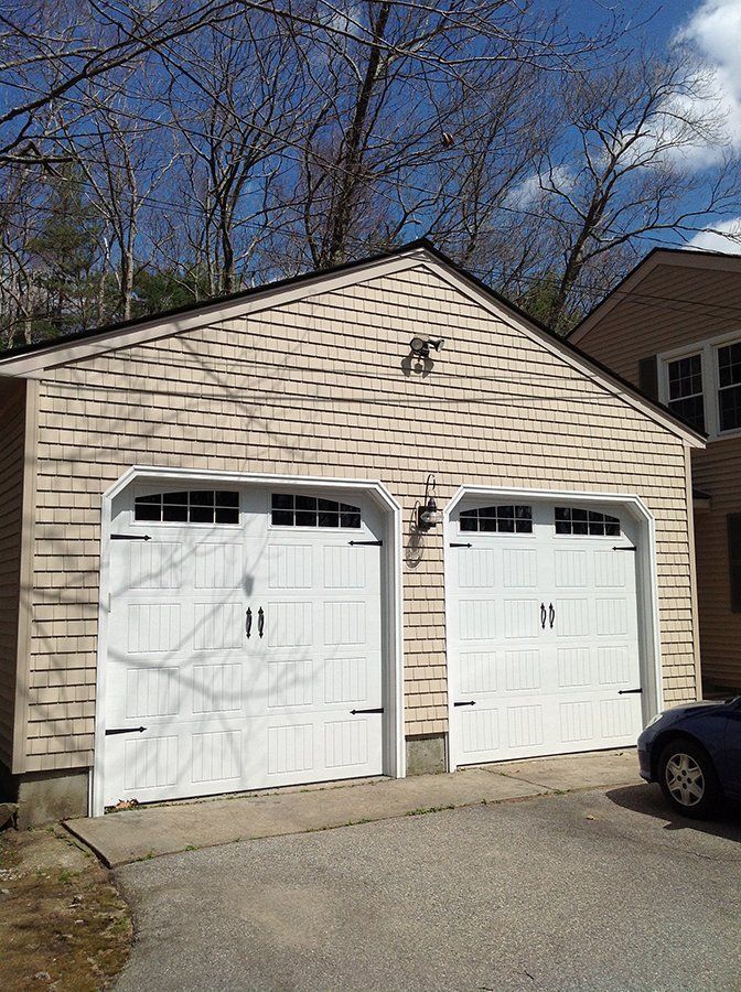 A car is parked in front of a garage with two white doors.