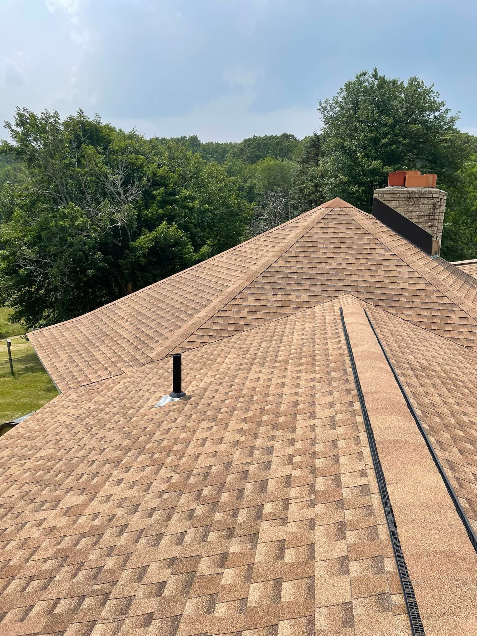 A close up of a roof with a chimney and trees in the background.