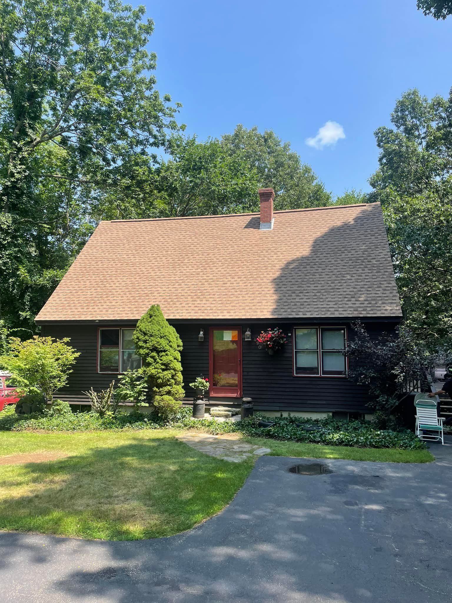 A small house with a brown roof and a red door is surrounded by trees.