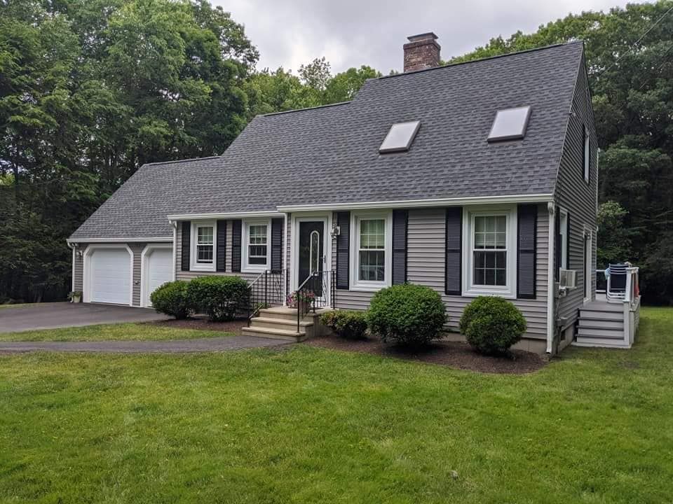 A house with a gray roof and black shutters is in the middle of a lush green field.