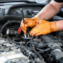 A man wearing orange gloves is working on a car engine.