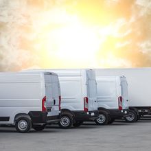 A row of white vans are parked in a parking lot.