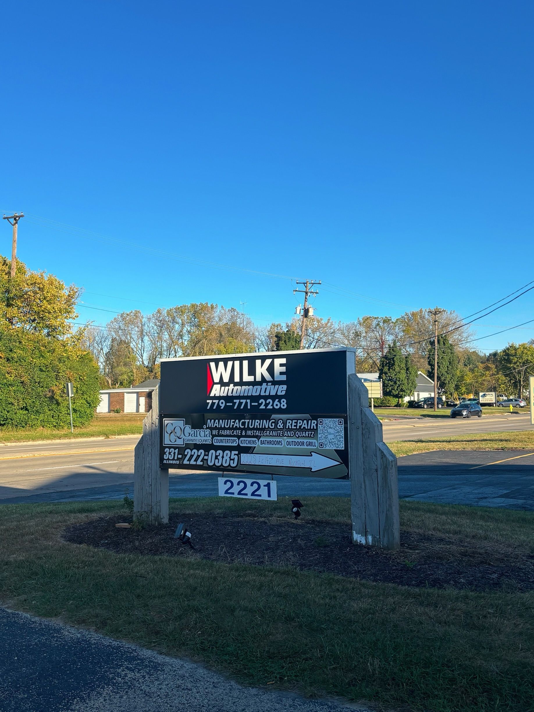 A sign for wilke automotive is sitting on the side of the road.