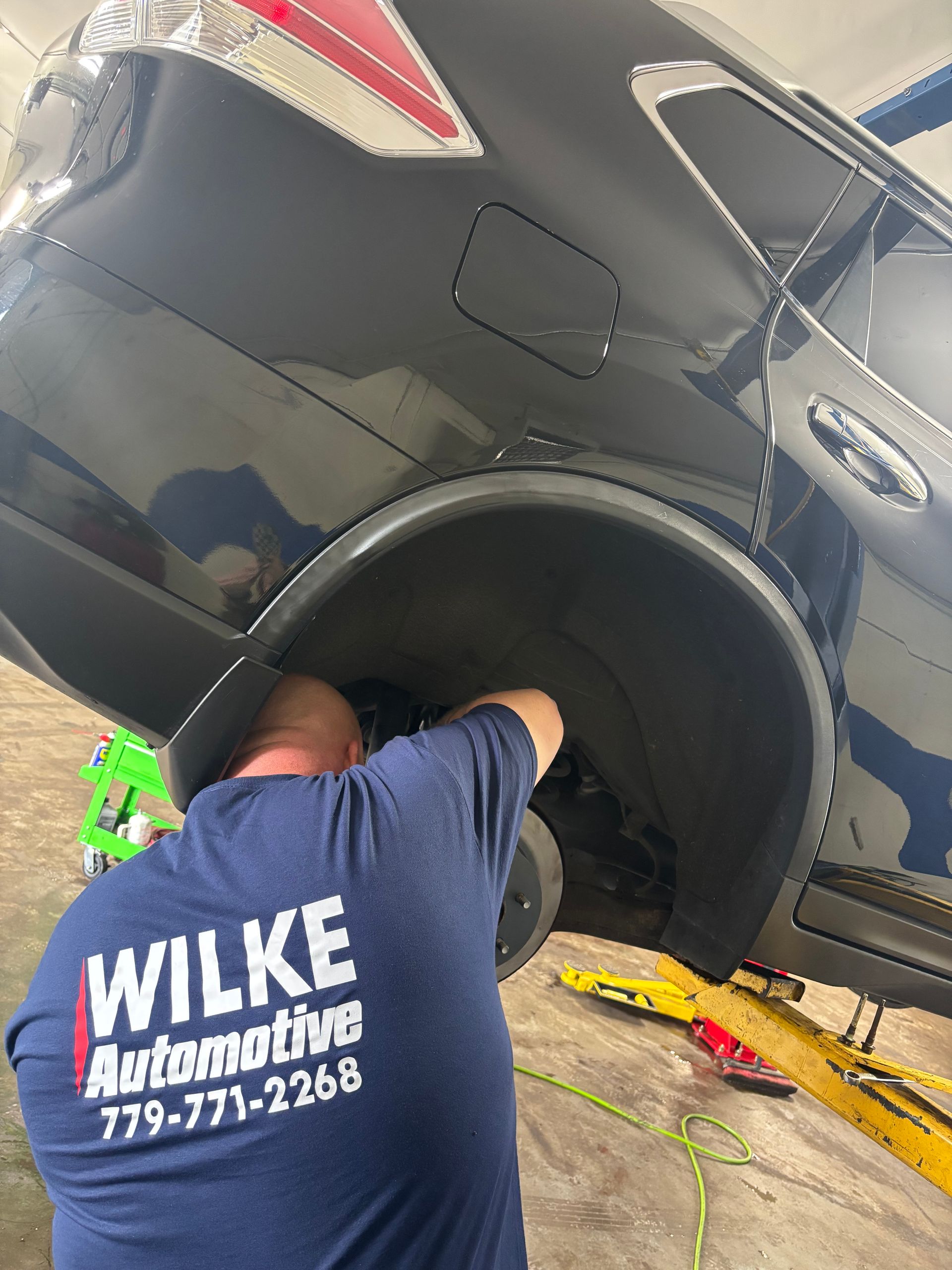 A man in a blue shirt is working on a black car.