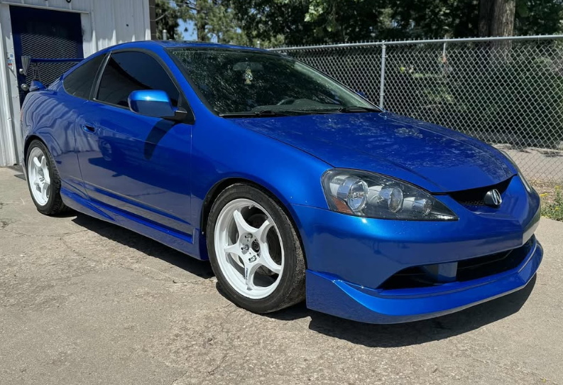 Blue Honda Integra coupe with white rims parked outside.