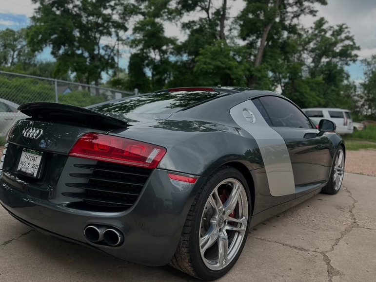 Dark gray Audi R8 sports car with a silver side stripe parked outside.