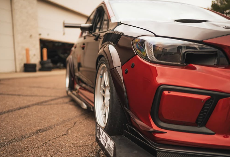 Red and black modified Subaru WRX with wide fender flares and aftermarket wheels, parked on asphalt.
