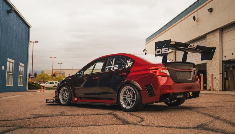 A modified black and red Subaru sedan with a large spoiler, parked near a building.