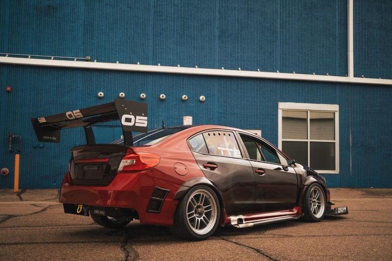 A red and black car is parked in front of a blue building.