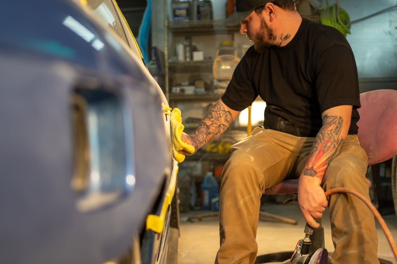A man is sitting in a chair polishing a car in a garage.