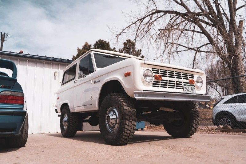 A white ford bronco is parked in a parking lot next to a blue car.