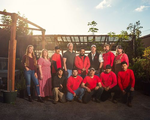 Group of people in red jackets posing outdoors in a garden under warm sunlight
