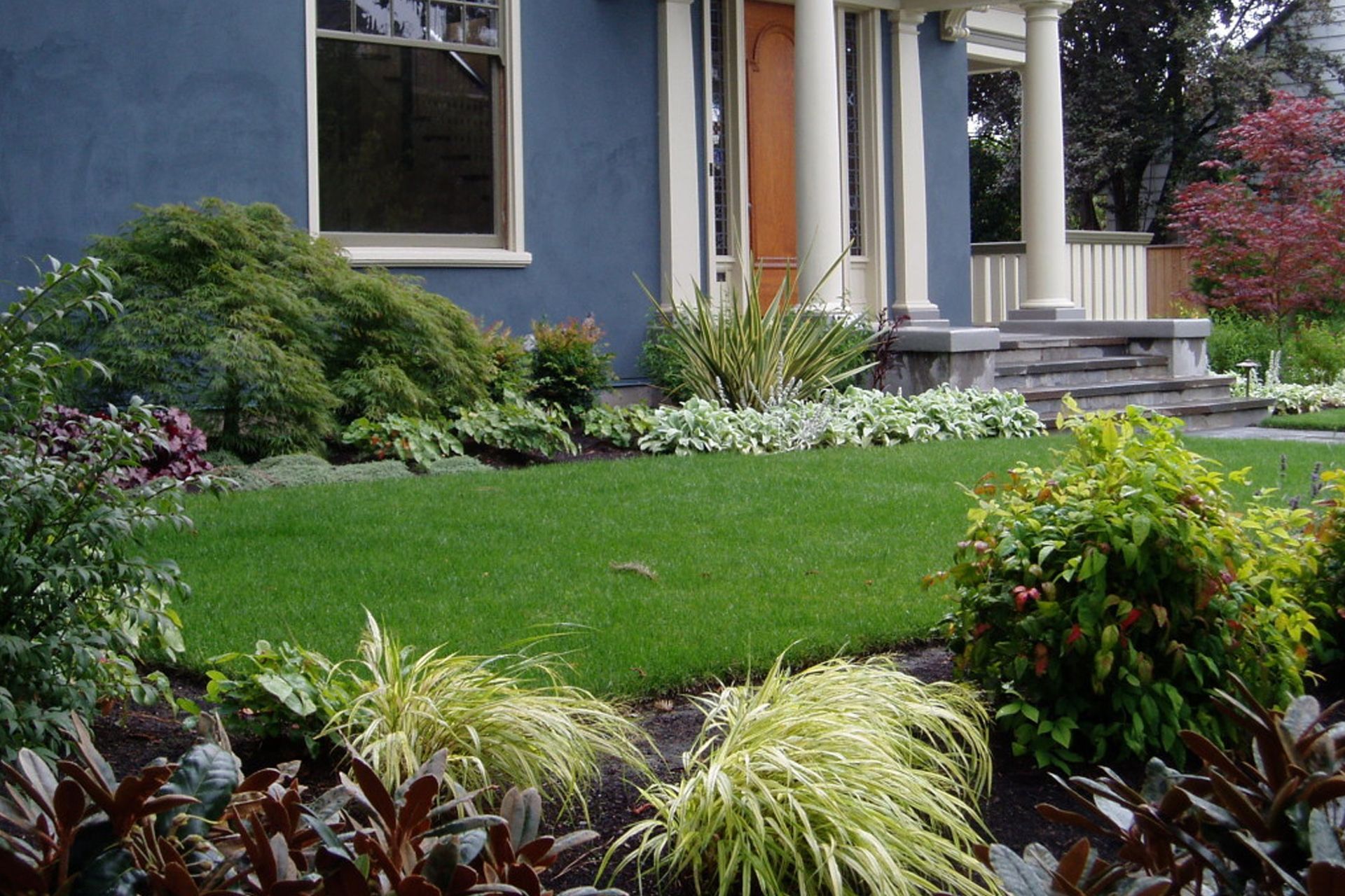 Blue house with white columns and a manicured green lawn and garden beds
